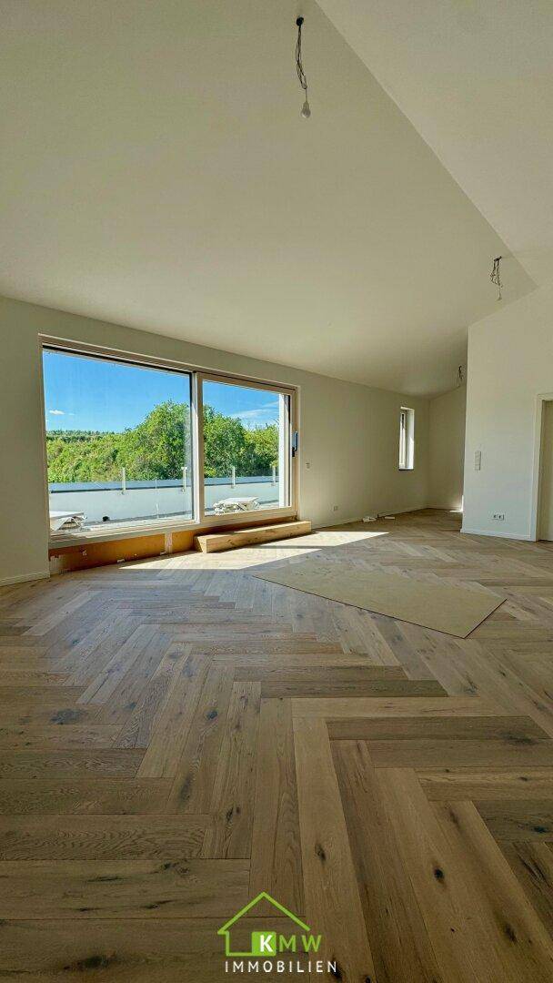 Geräumiger Wohnraum mit großen Fenstern, Fischgrätparkett und Blick ins Grüne.