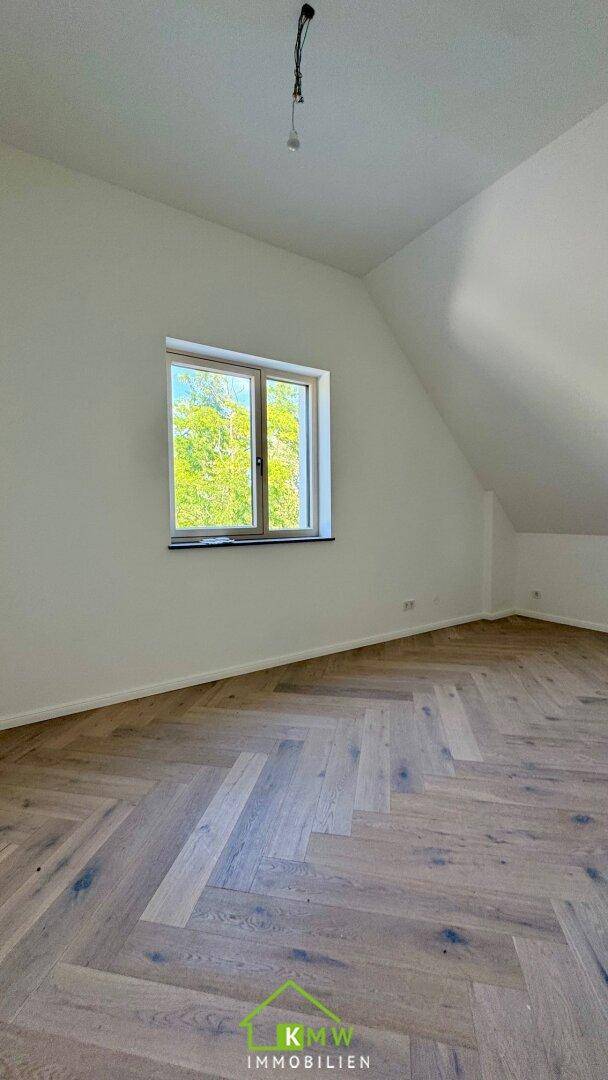 Helles Zimmer mit Fischgrätparkett, Dachschräge und einem Fenster mit Blick ins Grüne.