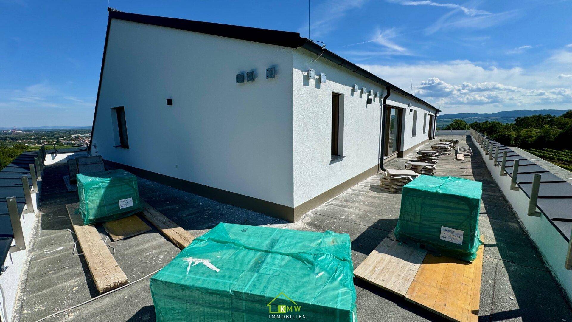 Außenansicht des Neubaus mit Dachterrasse in Bau und weitem Blick auf die Weinberge.