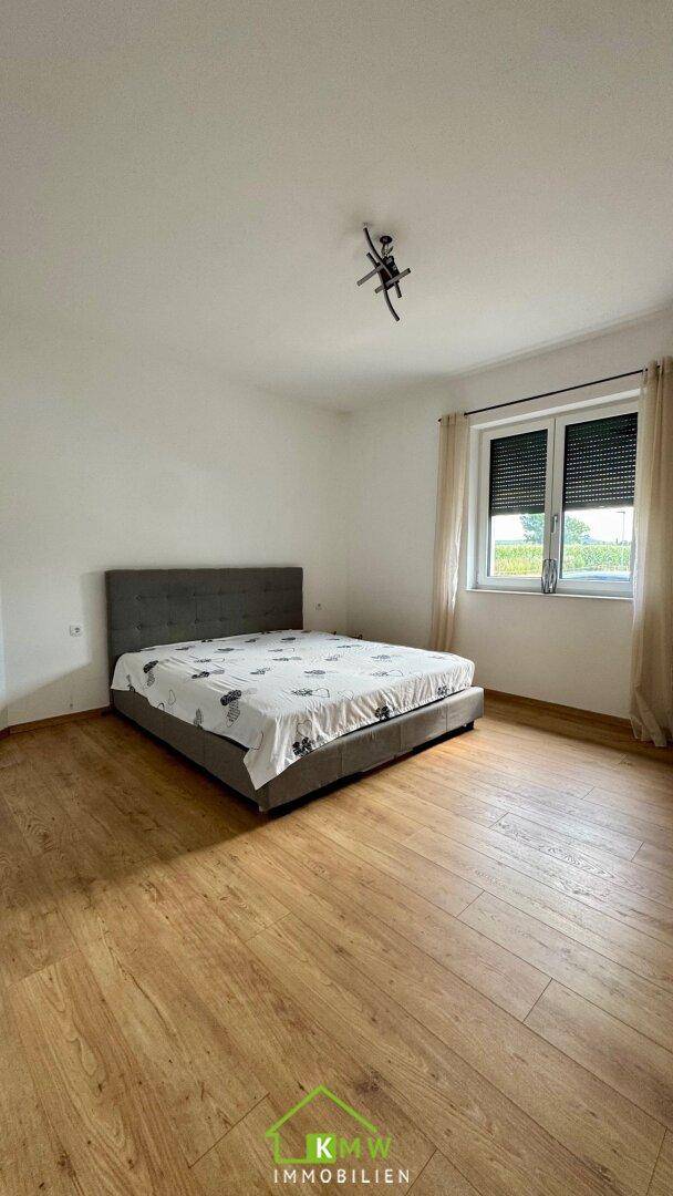 Schlafzimmer mit Holzboden, großem Bett und Fenster mit Blick ins Grüne.