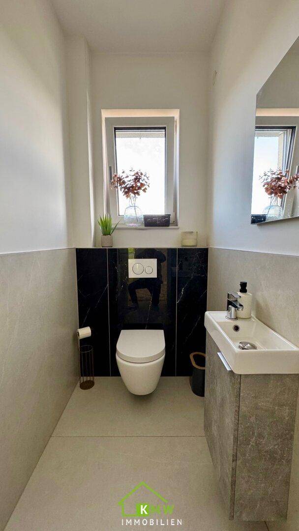 Modernes Gäste-WC mit wandhängendem WC, kleinem Waschbecken und Fenster.