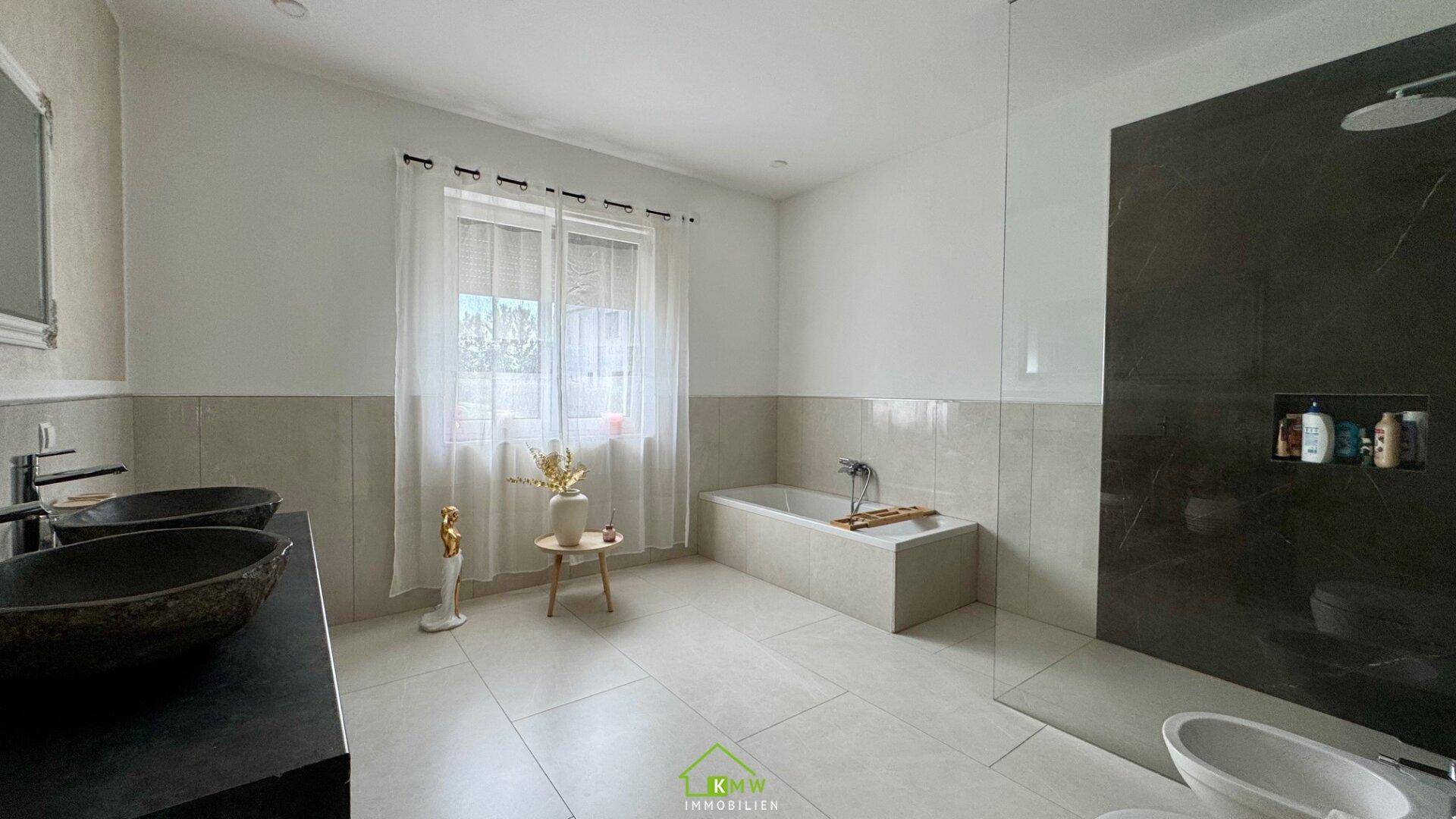 Helles Badezimmer mit Doppelwaschbecken, Badewanne und Fenster für Tageslicht.