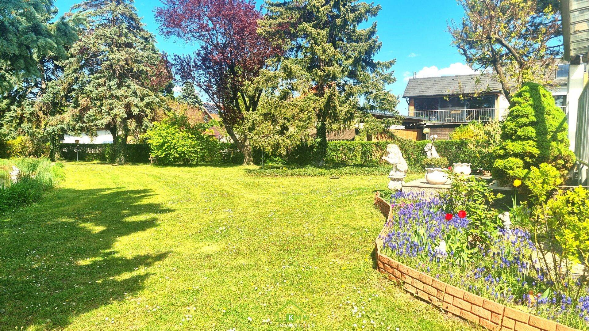 Gepflegter großer Gartenbereich mit blühenden Blumenbeeten und weitläufiger Rasenfläche.