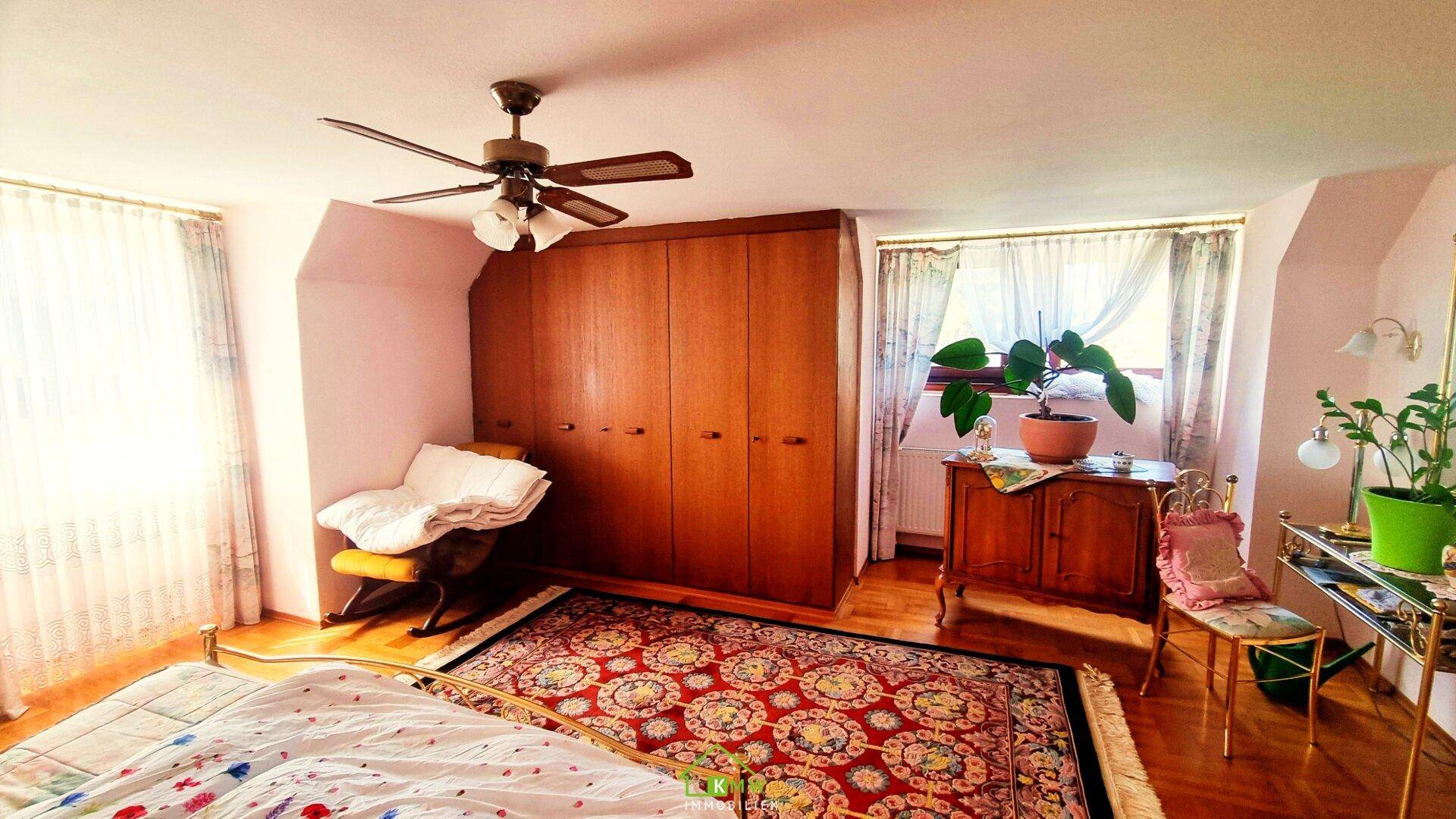 Helles Schlafzimmer mit Holzboden, Einbauschränken und Deckenventilator unter Dachschräge.
