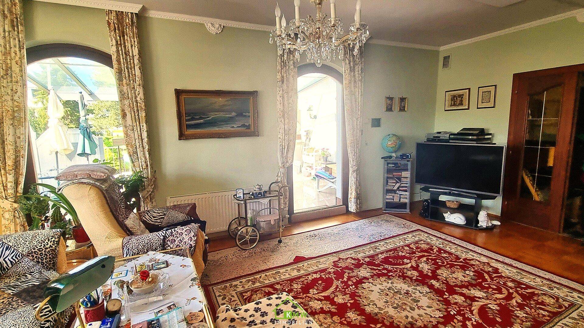 Geräumiges Wohnzimmer mit Kronleuchter, Parkettboden und Zugang zum Wintergarten.