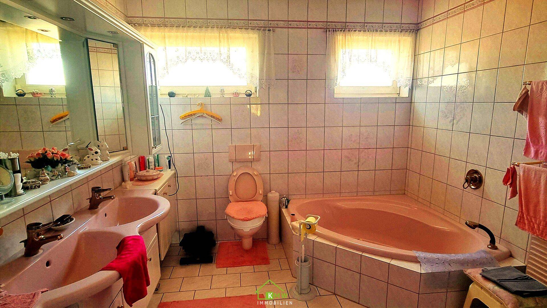 Badezimmer im 80er-Jahre-Stil mit rosa Badewanne, Doppelwaschbecken und Fliesen.