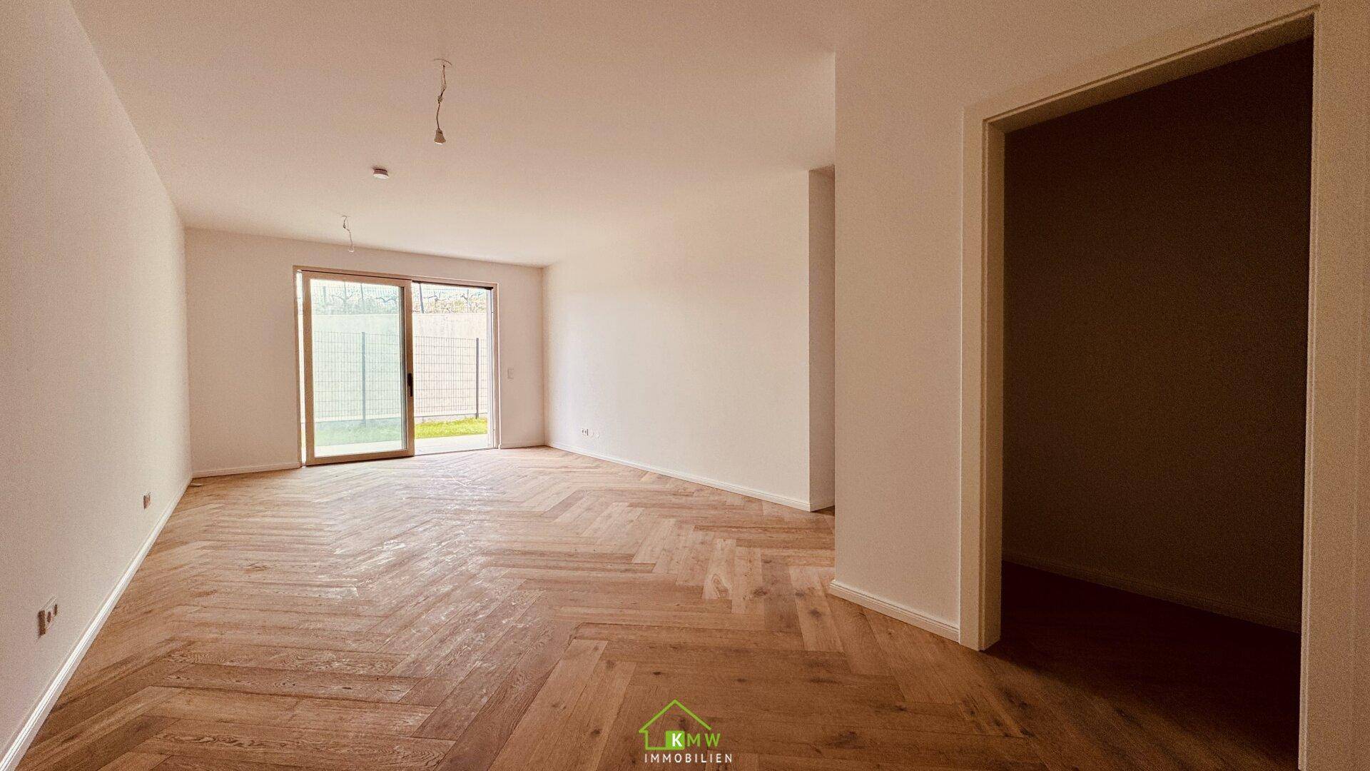 Helles, leeres Wohnzimmer mit elegantem Fischgrätparkett und Zugang zum Gartenbereich.