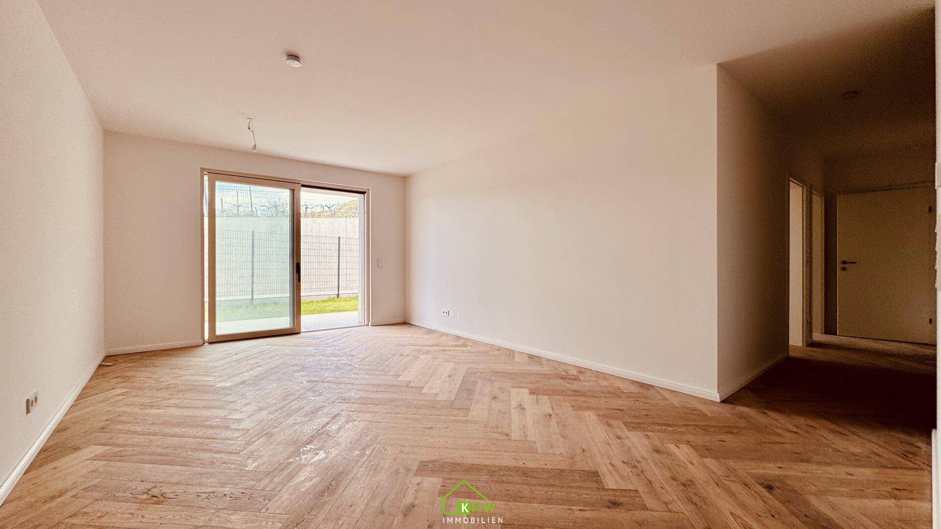 Geräumiges Wohnzimmer mit neu verlegtem Fischgrätparkett und viel Tageslicht durch die Terrassentür.