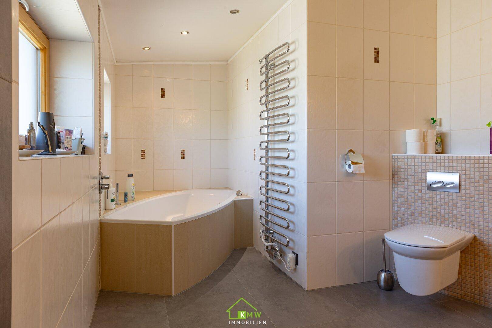Helles Badezimmer mit Eckbadewanne, beheiztem Handtuchhalter und wandhängendem WC.