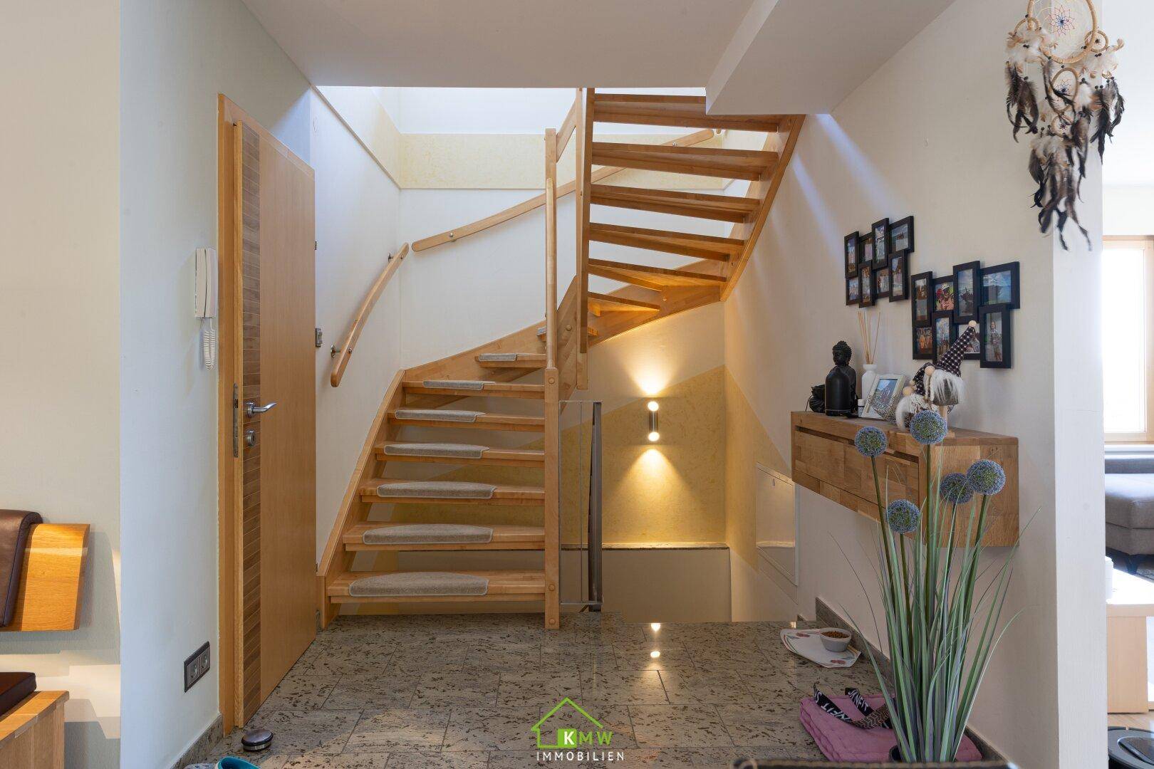 Heller Eingangsbereich mit Holztreppe, Fliesenboden und dekorativen Elementen.