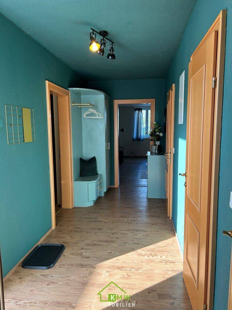Heller Flur mit türkisfarbenen Wänden, Holzboden und praktischer Garderobenlösung.