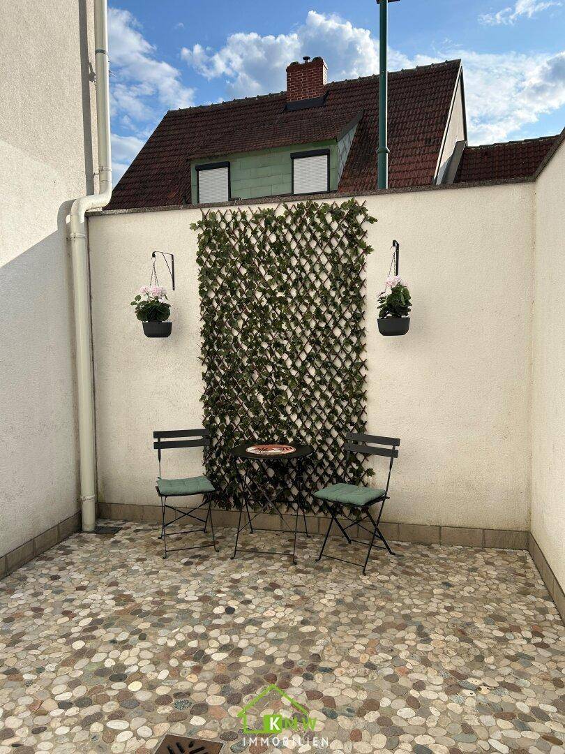 Kleiner gepflasterter Innenhof mit Sitzgelegenheiten und grüner Wanddekoration.