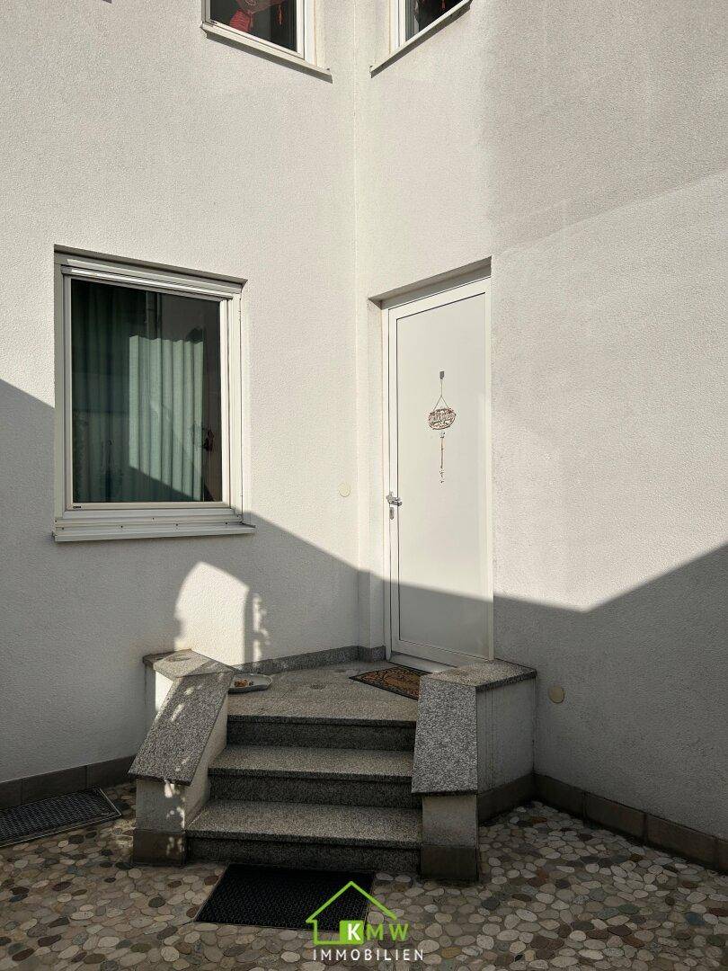 Eingangsbereich des Hauses mit Steinstufen und weißer Tür, umgeben von hellem Putz.