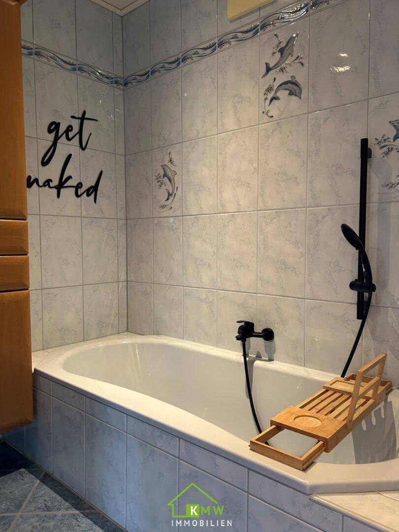 Badezimmer mit Badewanne, hellen Fliesen und modernen schwarzen Armaturen.