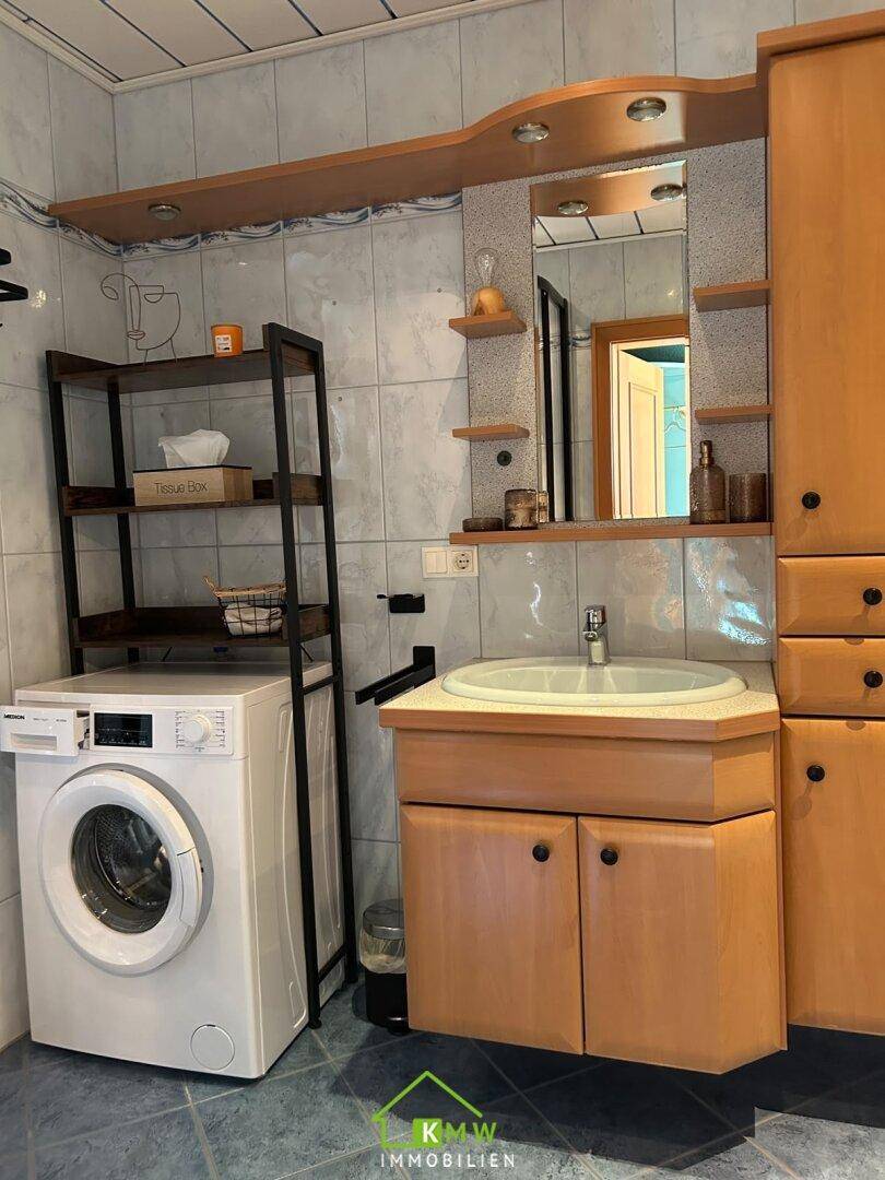 Funktionelles Badezimmer mit Waschmaschine, Waschbecken und praktischen Ablagemöglichkeiten.