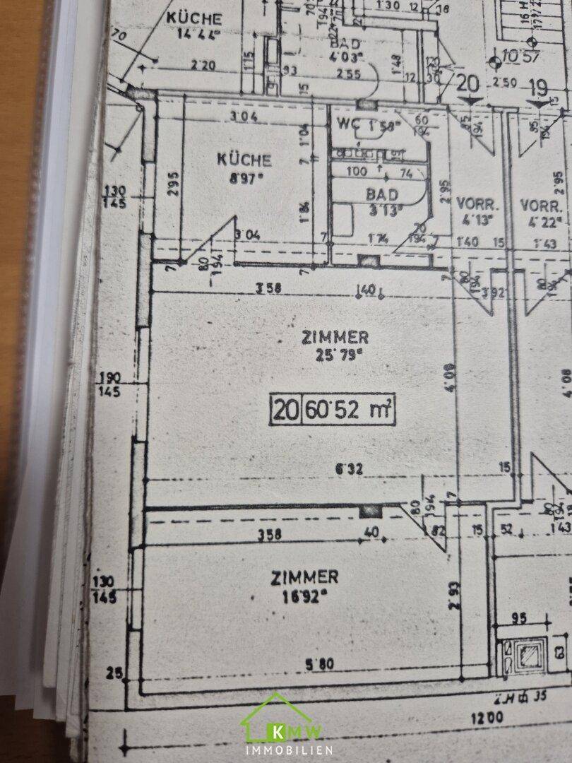 Detailansicht eines Grundrisses mit Küche, Bad und Zimmern, teilweise verdeckt und auf Papier abgebildet.