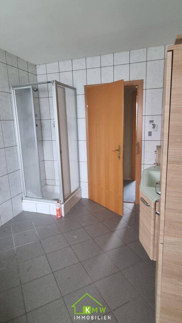 Badezimmer mit Duschkabine, Fliesenboden und hellen Wandfliesen.