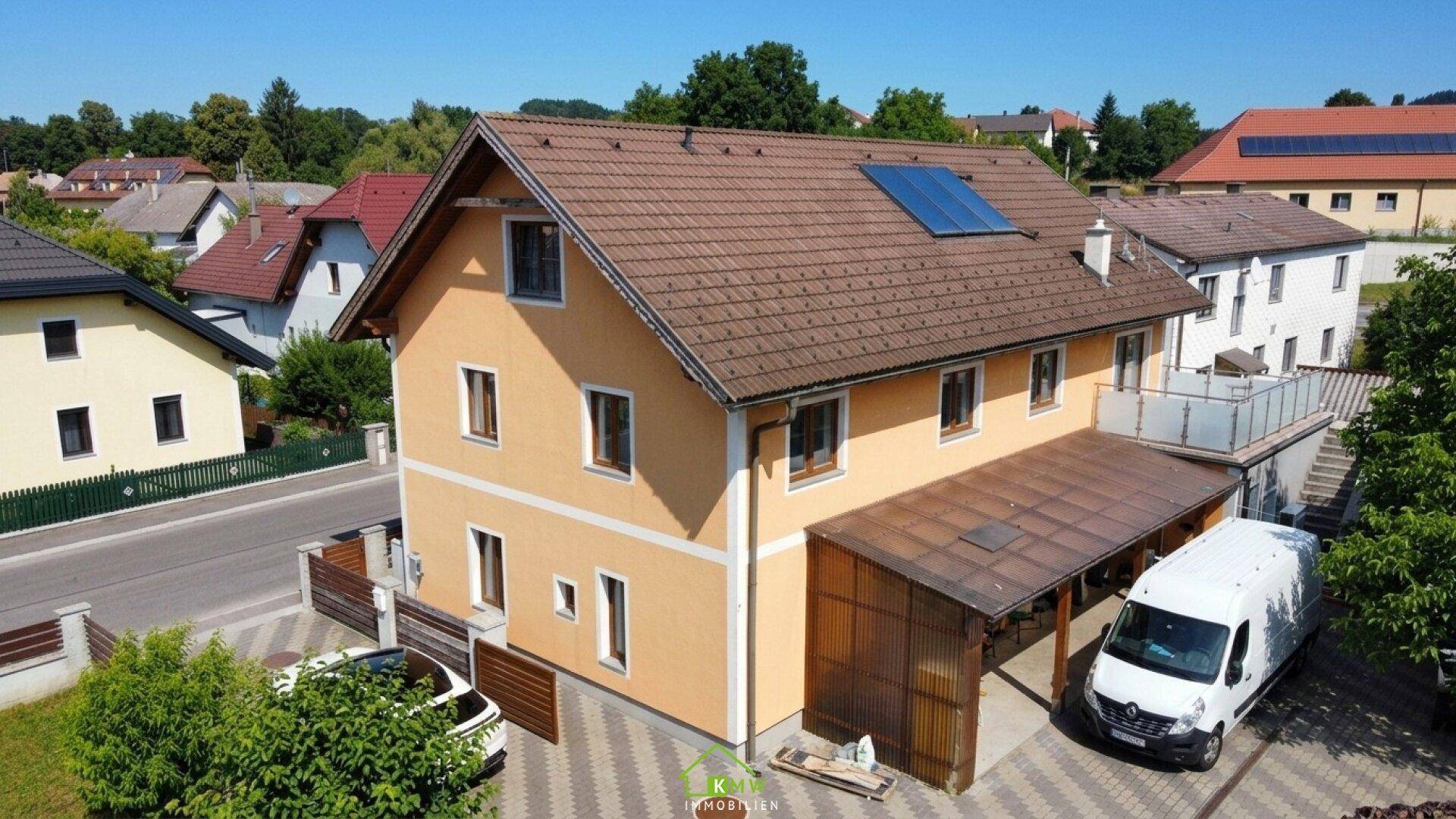 Ansicht des Hauses mit gelber Fassade, Carport und Solarpaneelen auf dem Dach.
