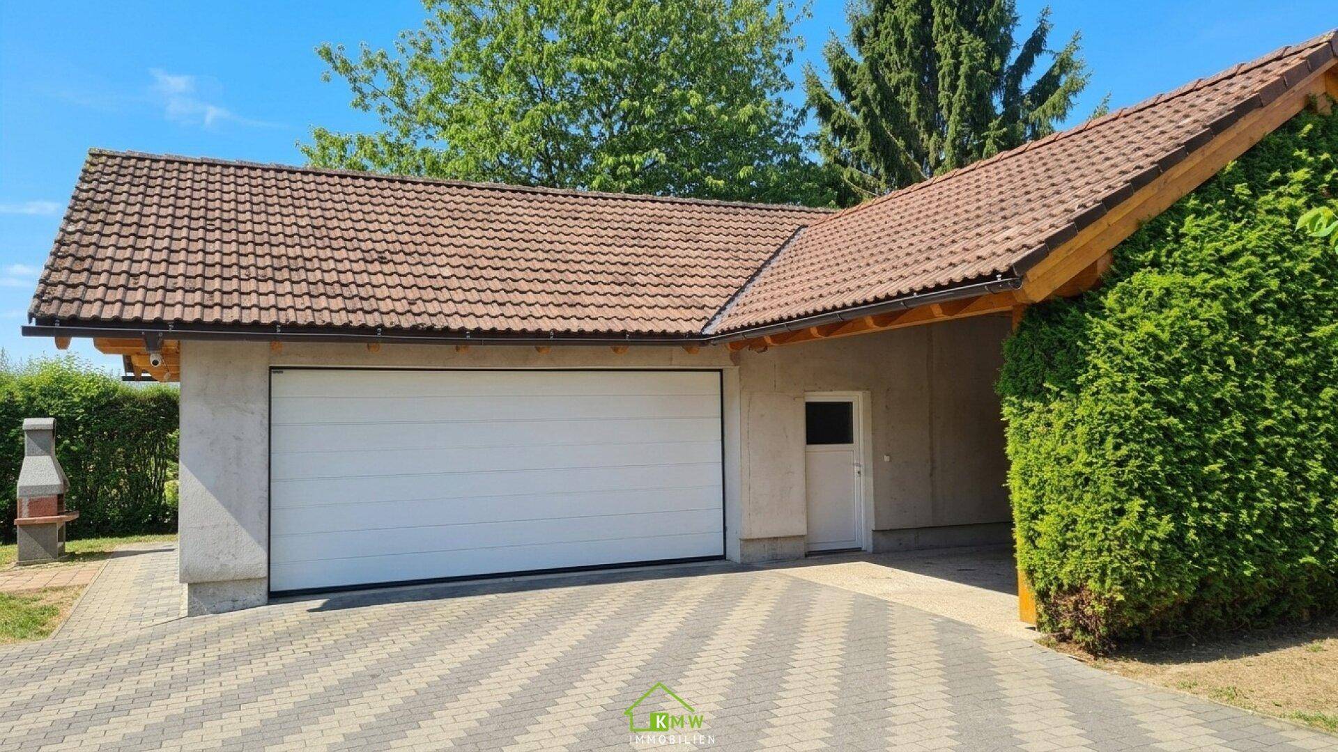 Doppelgarage mit weißem Tor und gepflasterter Zufahrt, umgeben von Hecken.