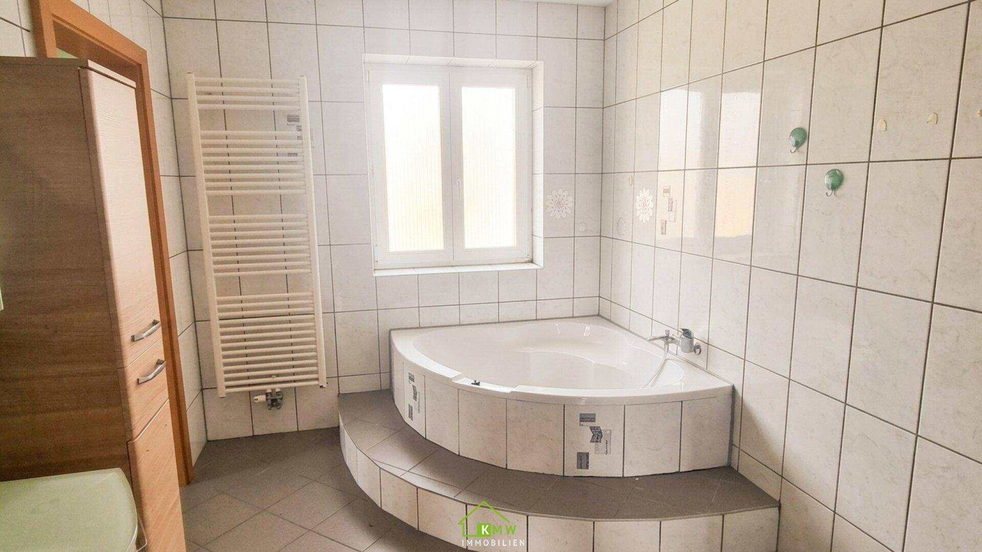 Badezimmer mit Eckbadewanne, beheiztem Handtuchhalter und Fenster.