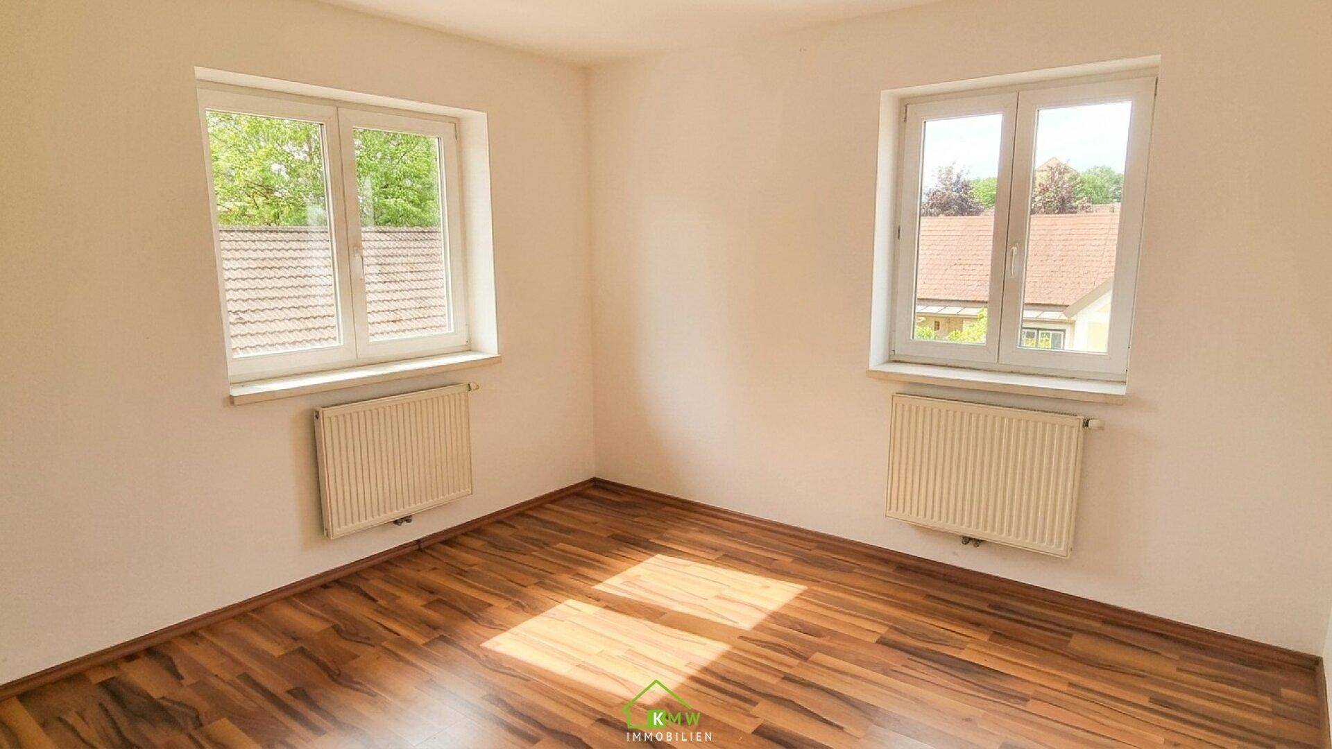 Helles Schlafzimmer mit Laminatboden, weißen Wänden und zwei Fenstern.