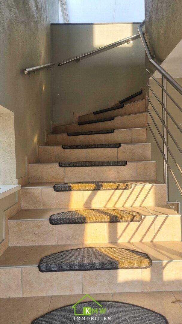 Geflieste Treppe mit Metallgeländer und Teppichstufen, hell beleuchtet.