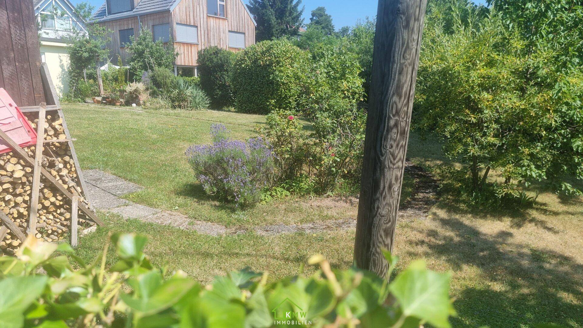 Idyllischer Garten mit Lavendelbüschen, Holzstapel und einem charmanten Haus im Hintergrund.