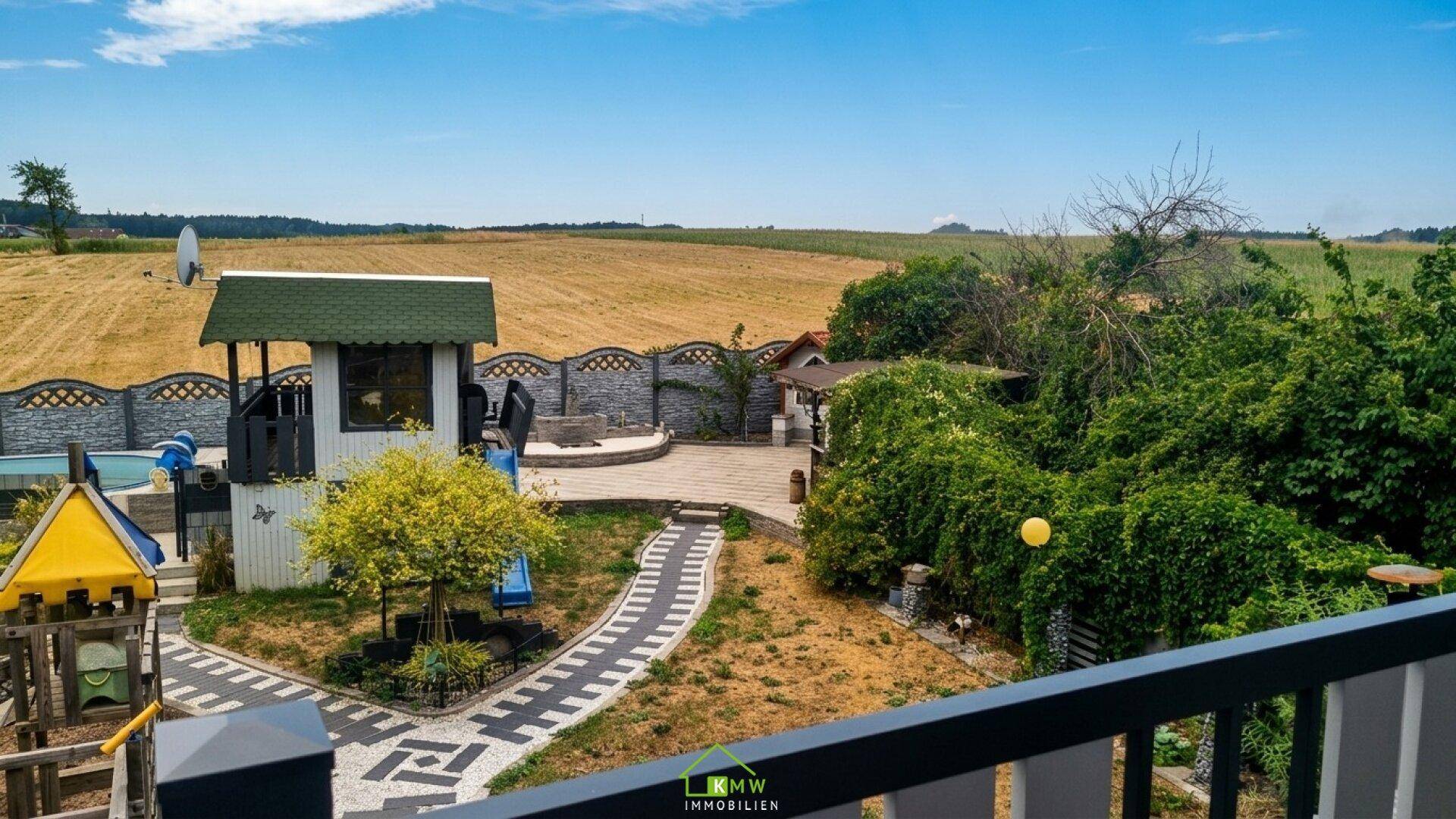 Weitläufiger Blick von einem Balkon auf den Garten, Spielplatz und die ländliche Umgebung.