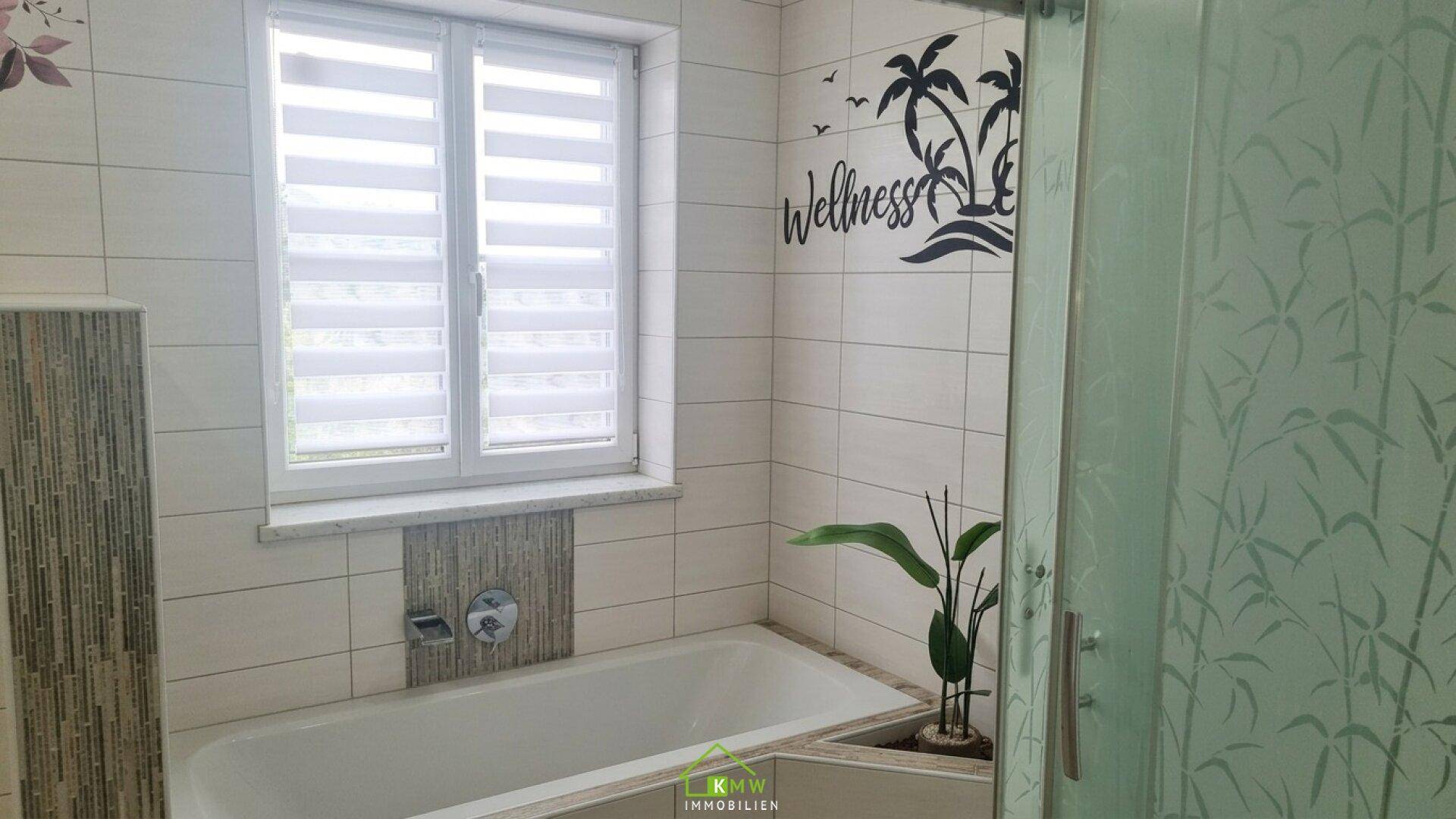 Badezimmer mit Badewanne, Duschkabine, Fenster und einer Wanddekoration im Wellness-Stil.