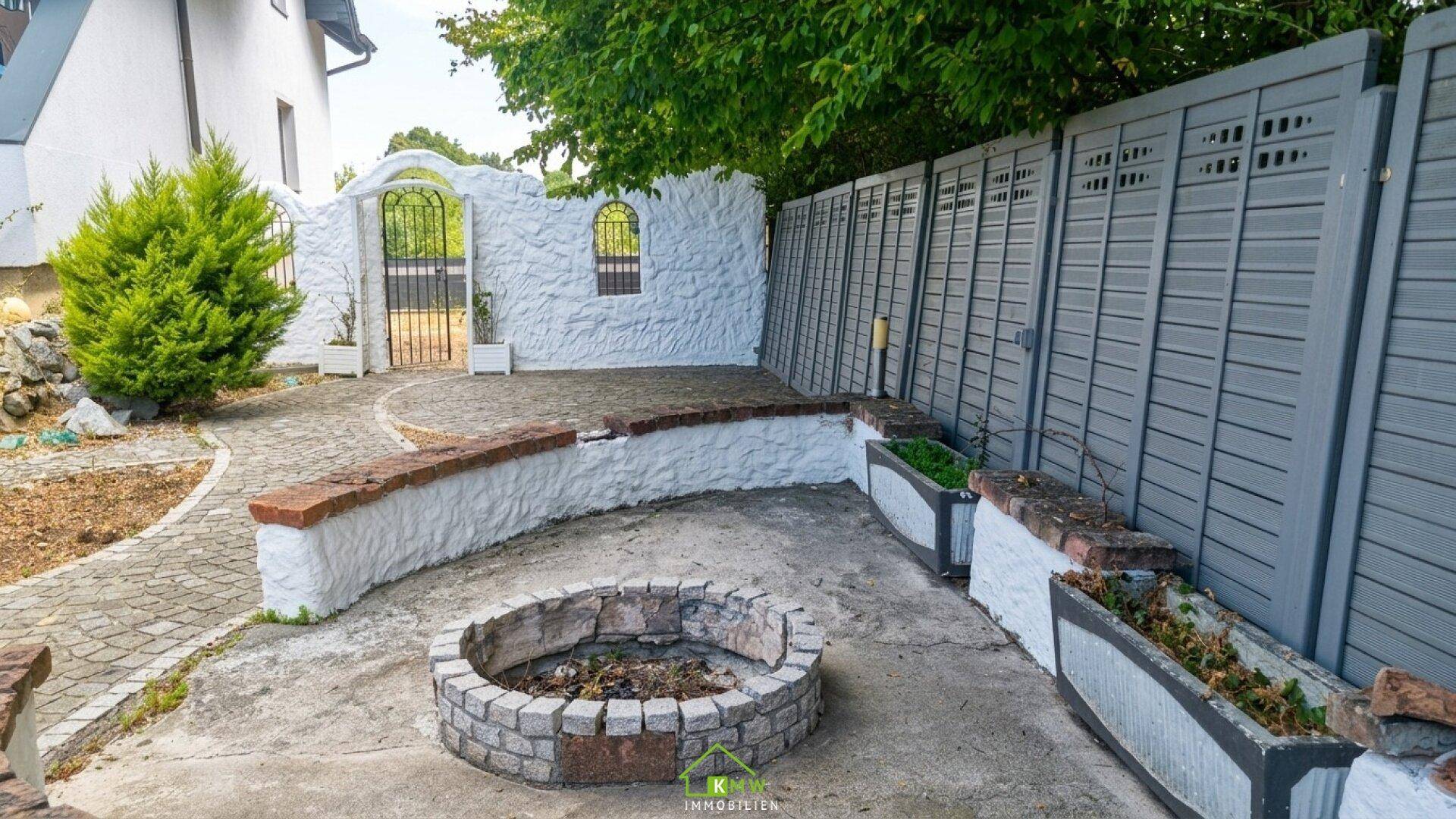 Gemütlicher Gartenbereich mit einer gemauerten Feuerstelle, Hochbeeten und einer Steinmauer.