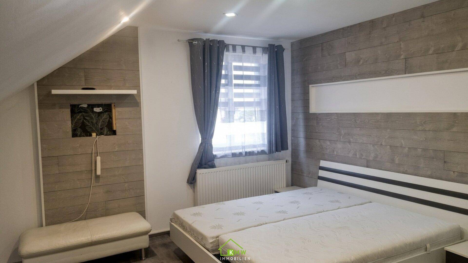 Schlafzimmer mit Holzwandverkleidung, Doppelbett und einem Fenster mit Jalousien.