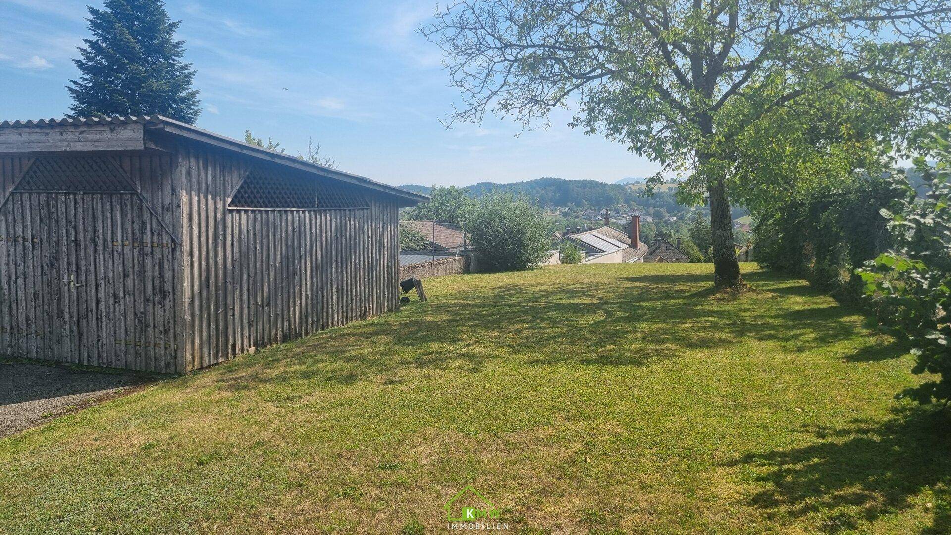 Große Rasenfläche mit einem Holzschuppen und Bäumen, bietet einen weiten Blick auf die umliegende Landschaft.