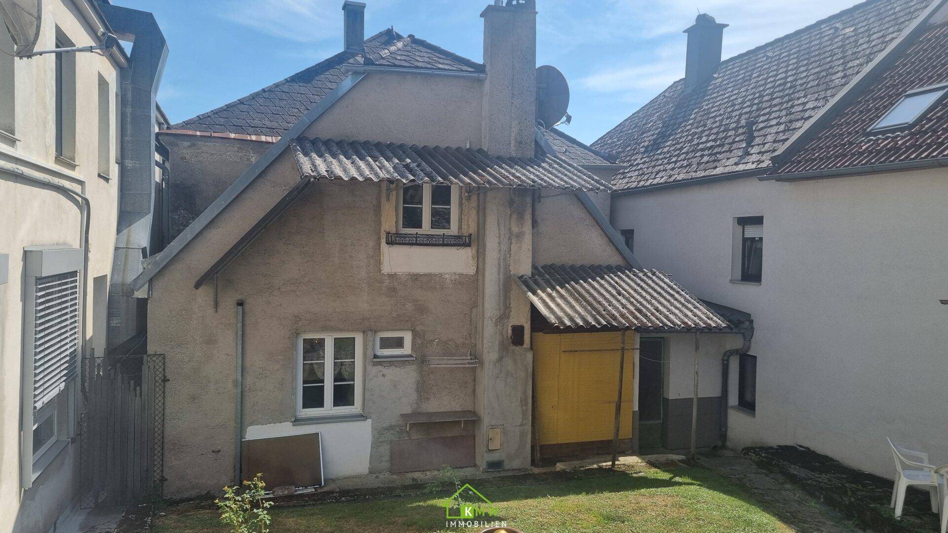 Rückansicht eines älteren Hauses mit einem kleinen Gartenbereich und einfacher Architektur.