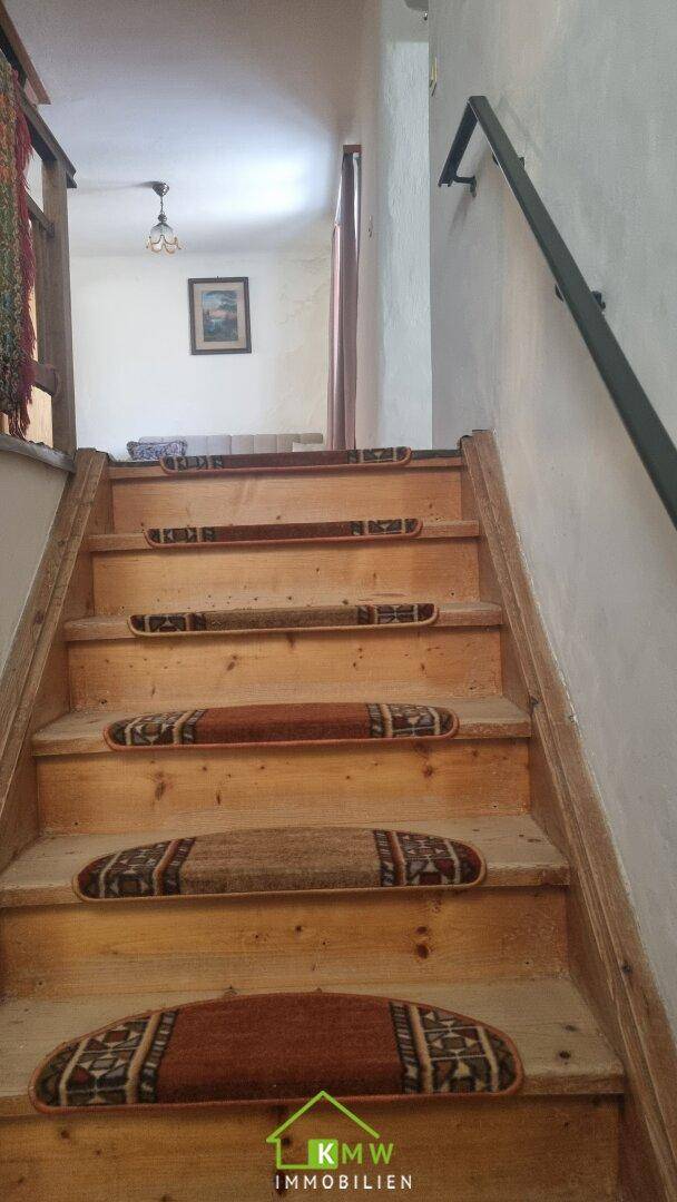 Holztreppe mit Teppichläufern, die in das obere Stockwerk führt, mit einem Handlauf an der Wand.