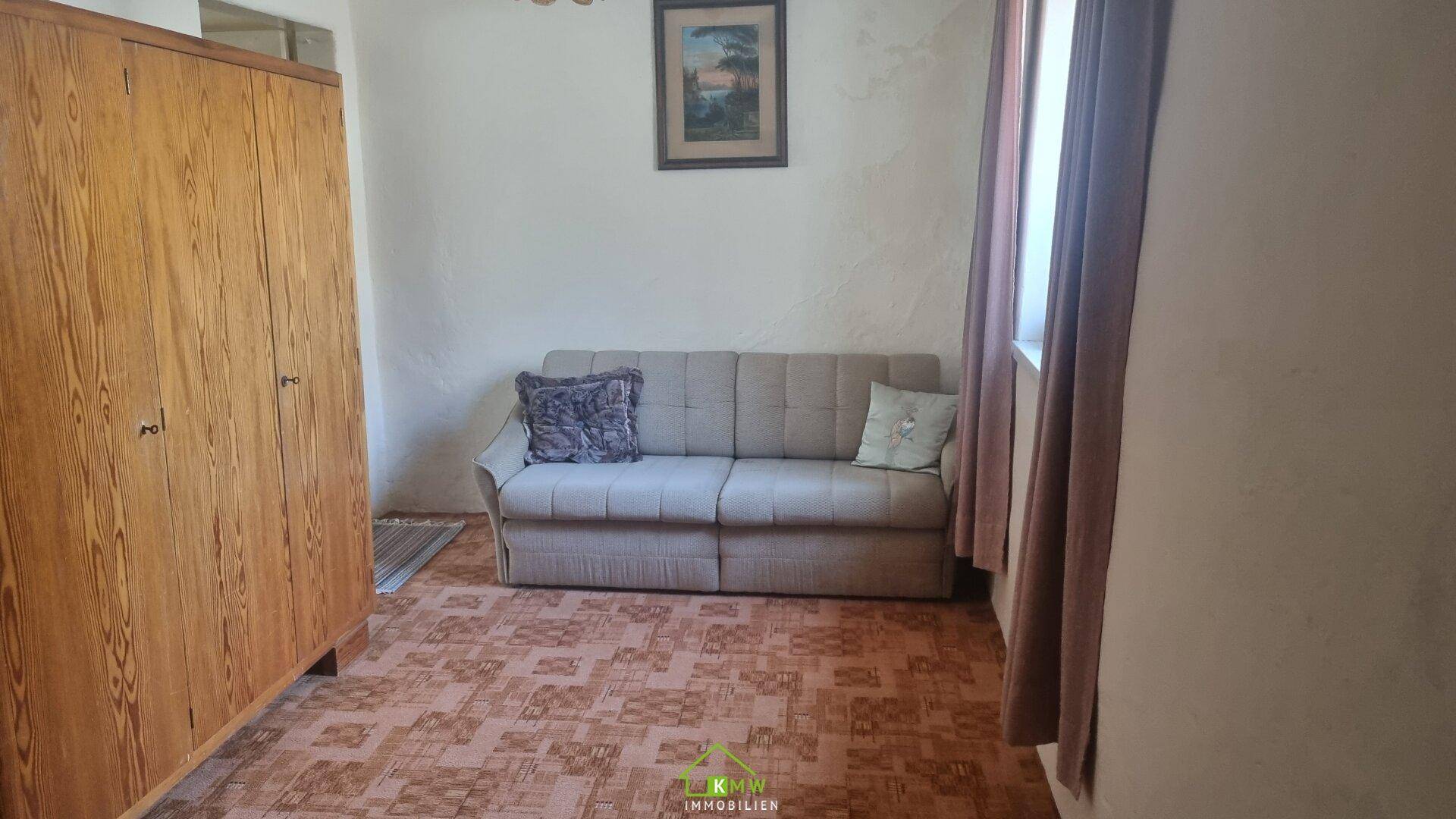 Zimmer mit einem Schlafsofa und einem großen Holzschrank, ausgestattet mit einem gemusterten Bodenbelag.
