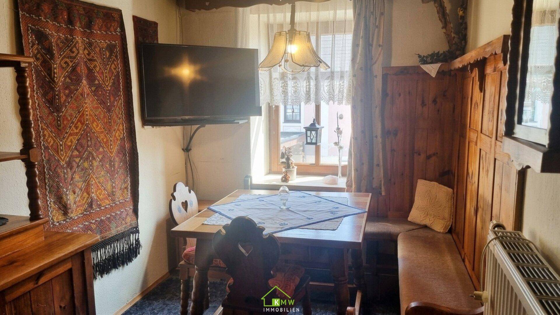 Gemütlicher Essbereich im alpinen Stil mit Holztisch, Eckbank und einem Fernseher an der Wand.