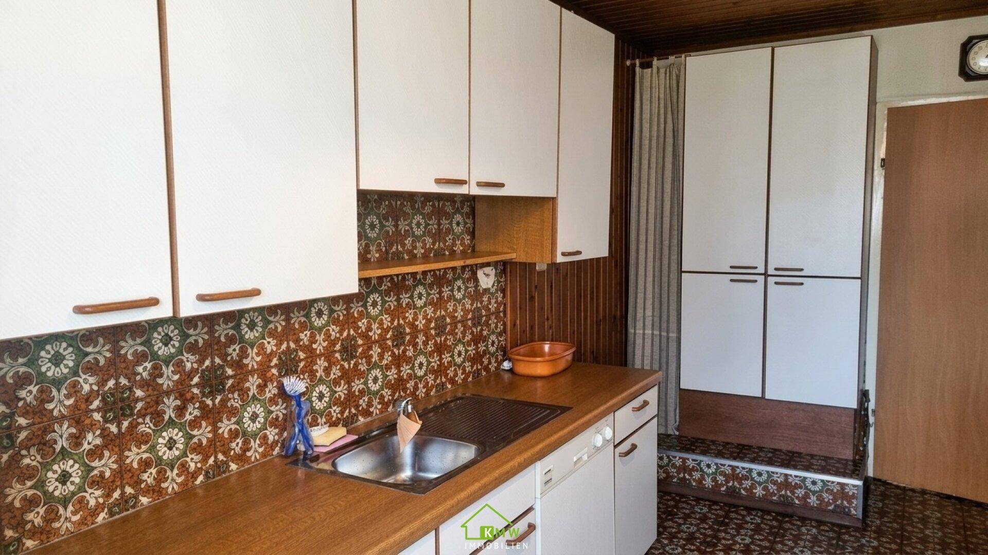 Ältere Küche mit weißen Schränken, gemusterten Fliesen und Holz-Arbeitsplatte, die eine traditionelle Atmosphäre schafft.