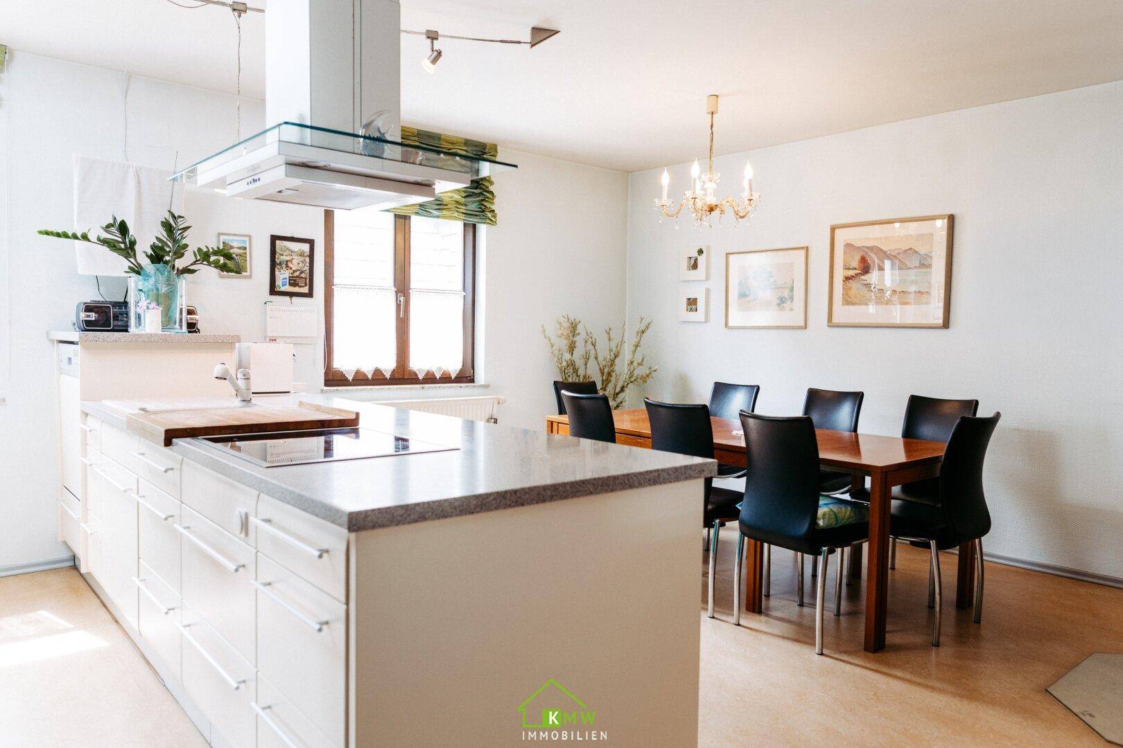 Geräumige Küche mit Kücheninsel, Essbereich und hellem Laminatboden, ideal für Familien.