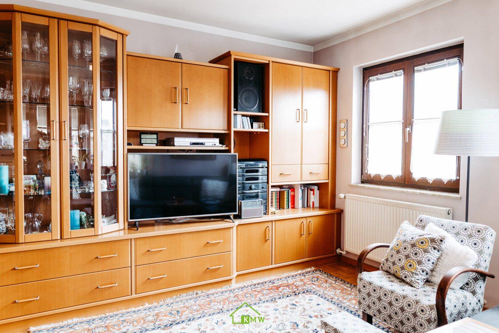 Wohnzimmer mit großer Wohnwand aus Holz, Fernseher und gemütlichem Sessel, ideal zum Entspannen.