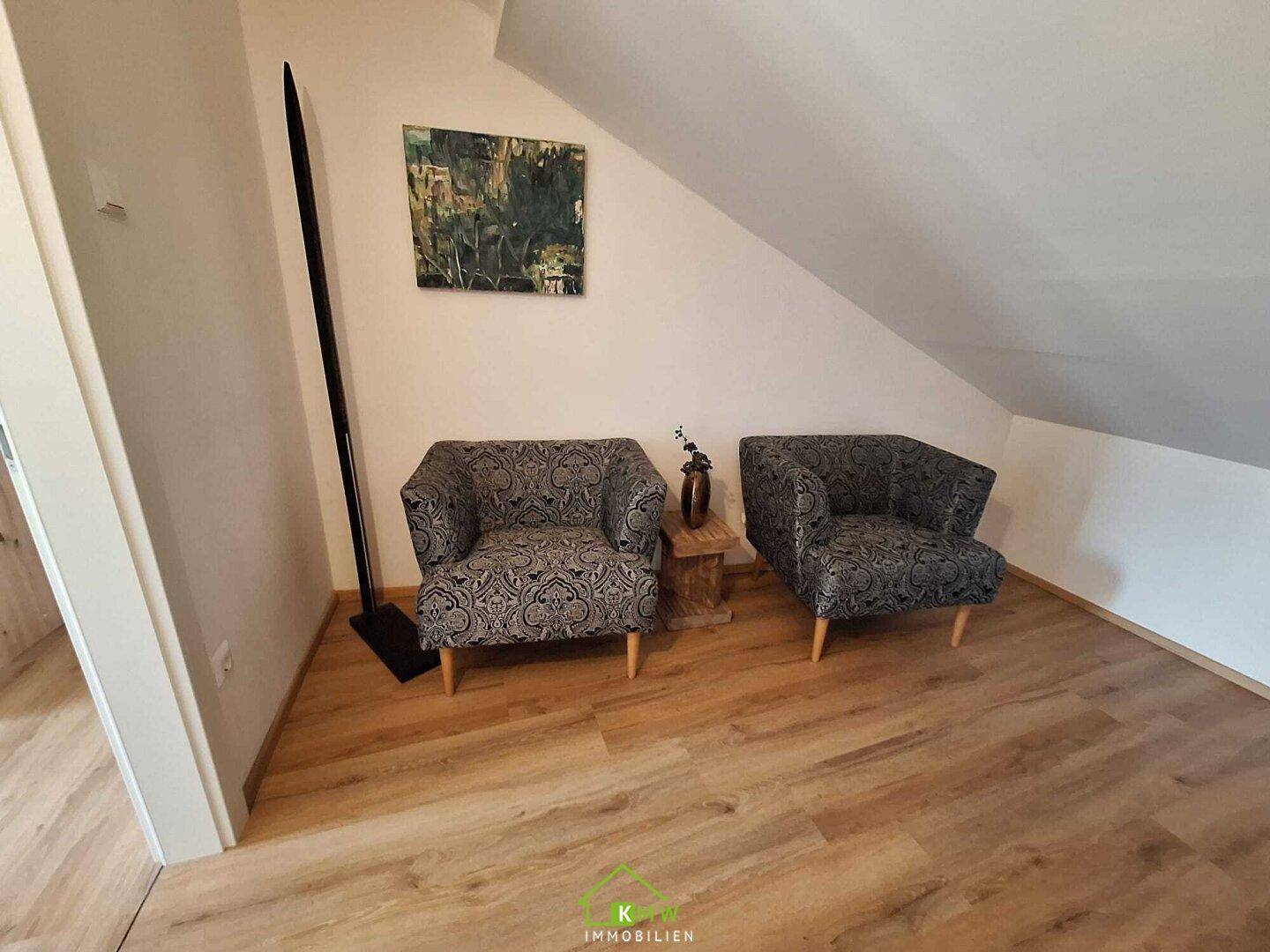 Gemütliche Sitzecke im Dachgeschoss mit zwei Sesseln, Holzboden und schräger Decke.