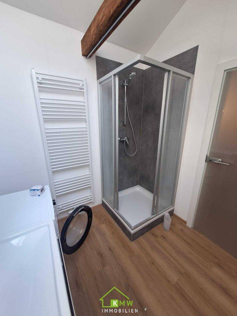 Badezimmer mit Duschkabine, beheiztem Handtuchhalter und Holzbalken im Dachgeschoss.