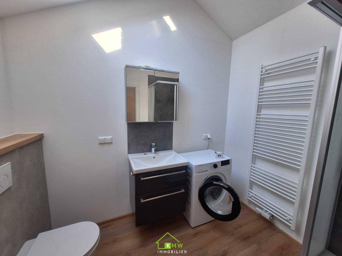 Modernes Badezimmer mit Waschbecken, Spiegelschrank, Toilette und Waschmaschine.
