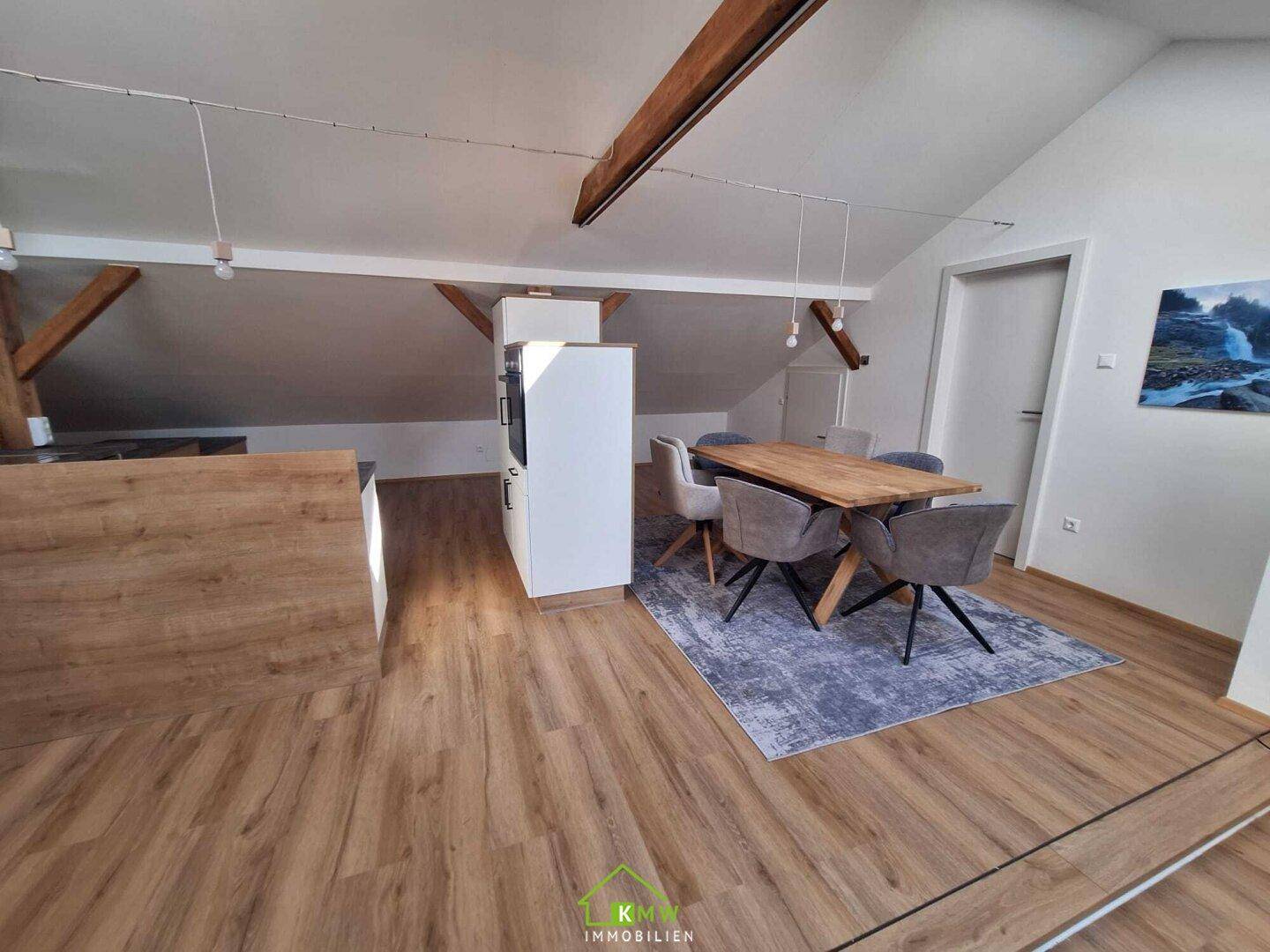 Heller Essbereich im Dachgeschoss mit großem Holztisch, modernen Stühlen und Holzbalken.