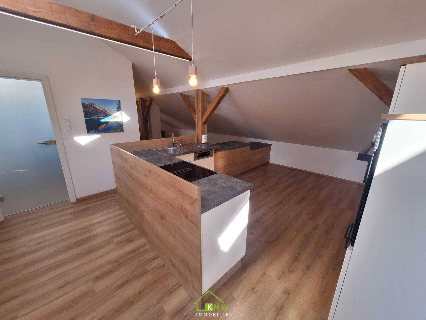 Moderne Einbauküche im Dachgeschoss mit Kochinsel, integrierten Geräten und Holzbalken.