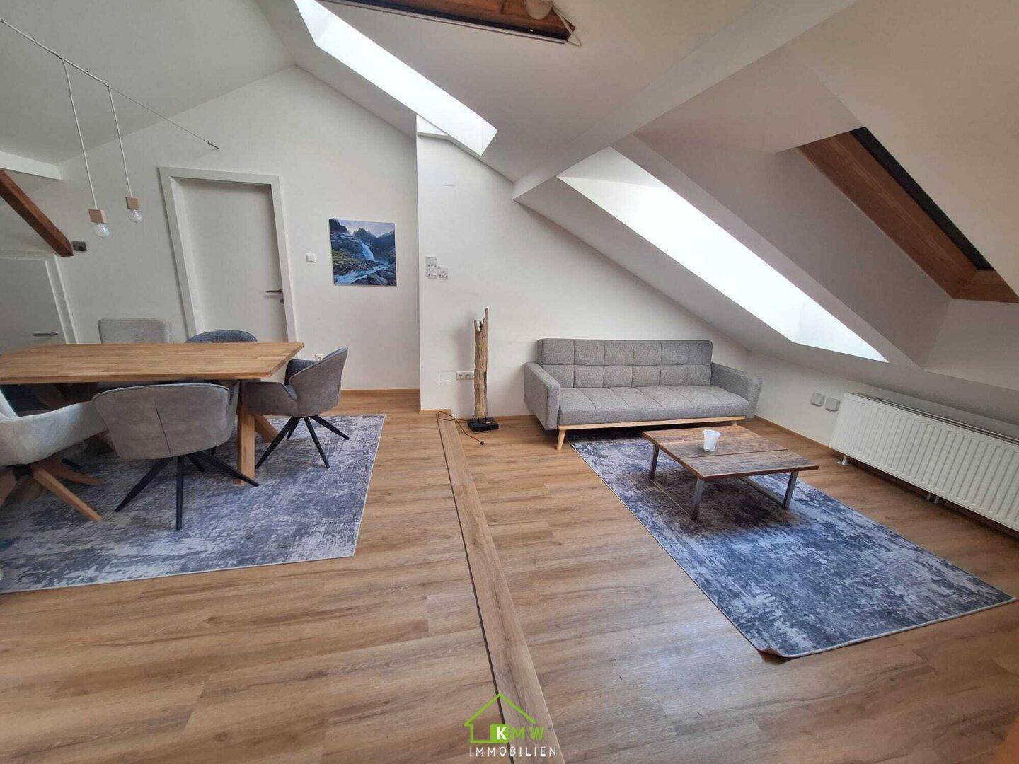 Geräumiger Wohn- und Essbereich im Dachgeschoss mit Holzboden, Esstisch und bequemer Couch.