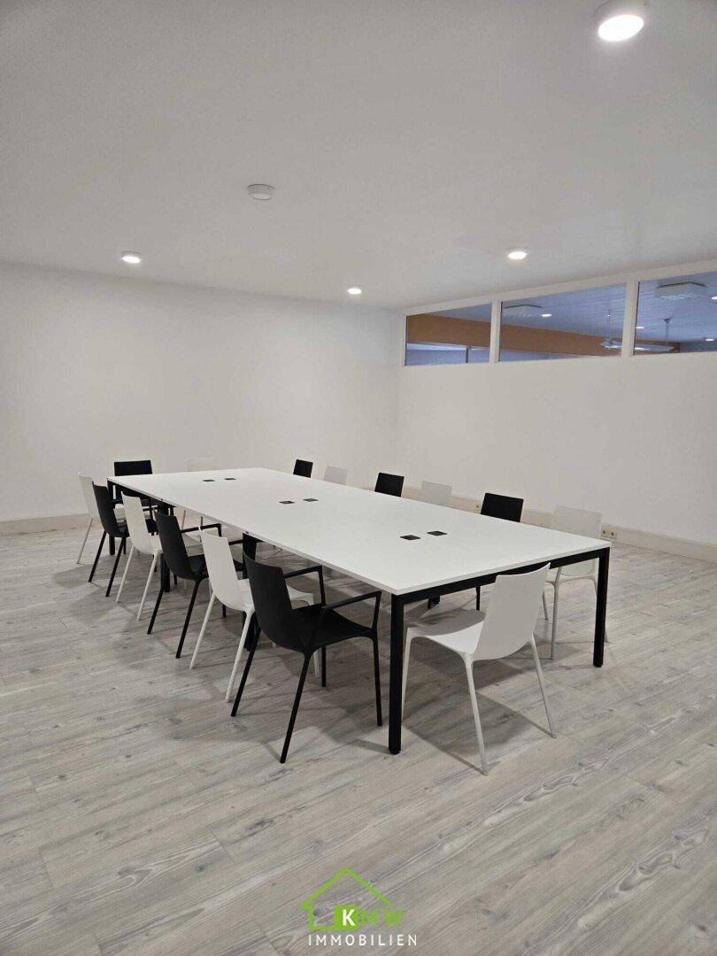Heller Konferenzraum mit langem Tisch, modernen Stühlen und hellem Laminatboden.