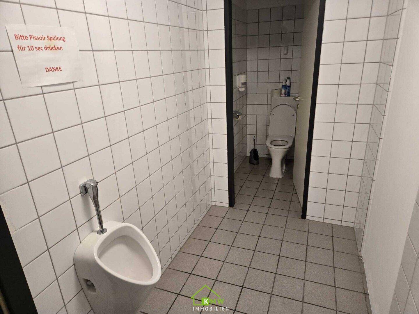 Herren-WC mit Urinal, gefliesten Wänden und separater Toilettenkabine, sauber und funktional.