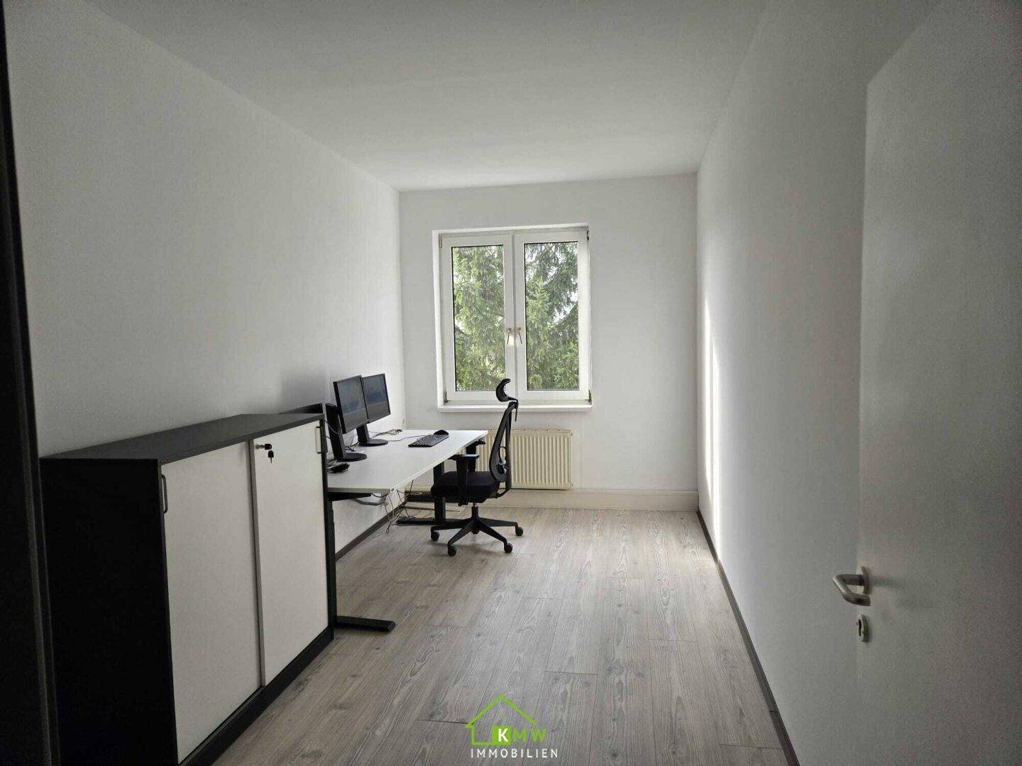 Funktionales Büro mit Schreibtisch, Bürostuhl, Aktenschränken und Fenster mit Blick ins Grüne.