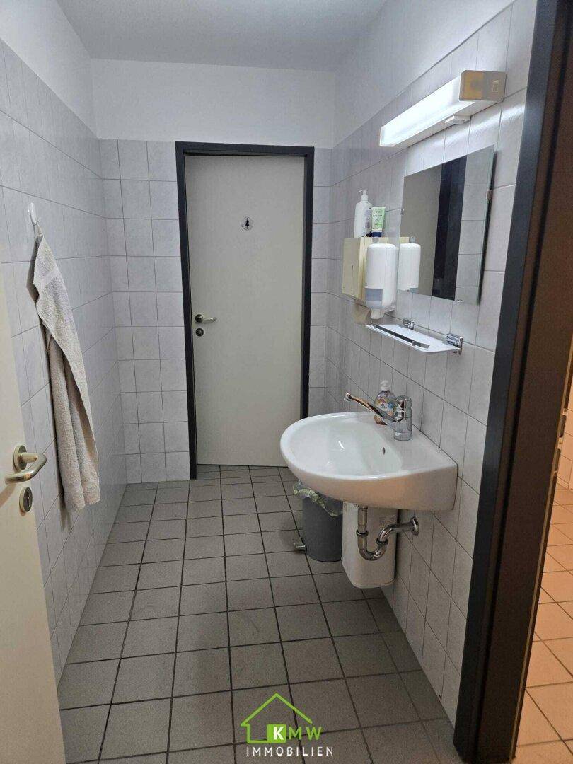 Gefliester Waschraum mit Waschbecken, Spiegel und Handtuchhalter, hell und gepflegt.