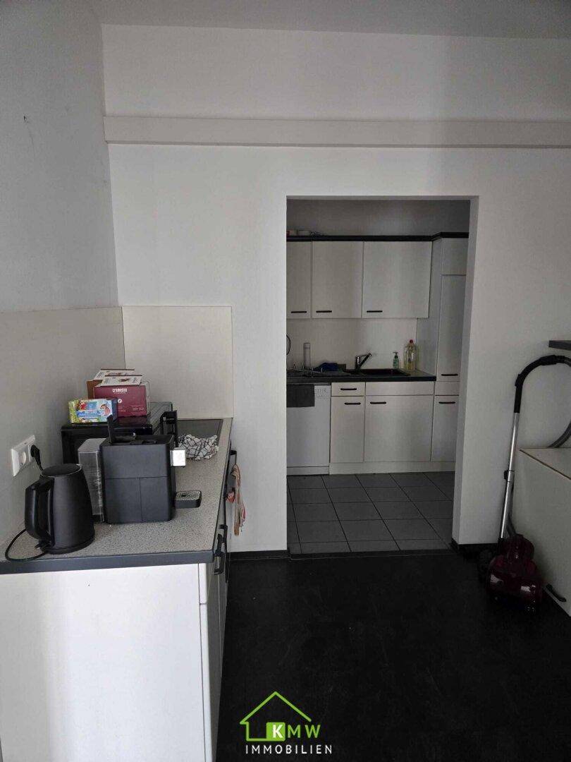 Kleine Küchenzeile mit weißen Schränken, Spüle und Kaffeemaschine, ideal für Pausen.